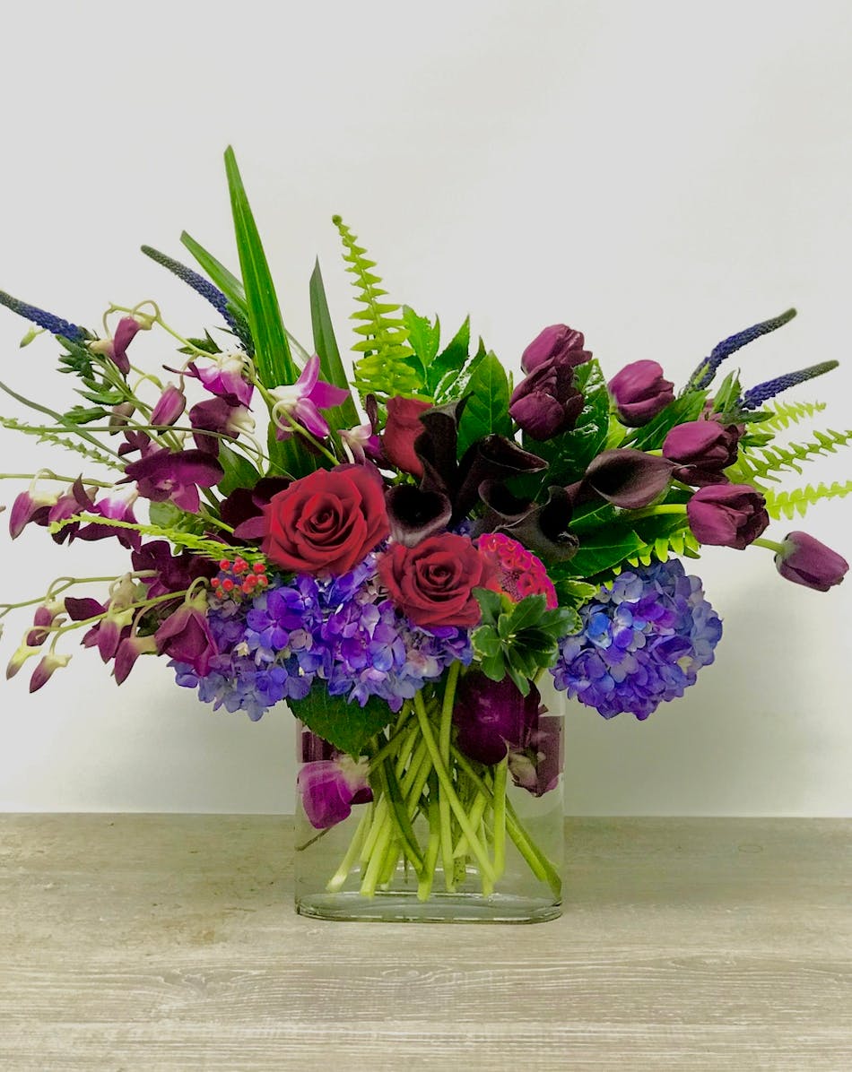 Flowers in purples, reds and blues in a clear glass vase. 